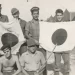 Ο George Burlotos όρθιος, δεύτερος από δεξιά, ποζάρει με ορισμένους συναδέλφους του, κρατώντας ως λάφυρα δύο Ιαπωνικές σημαίες και ένα ξίφος αξιωματικού. Την μία εξ’ αυτών την έφερε μαζί του πίσω στις ΗΠΑ, ως αναμνηστικό της θητείας του στην Okinawa. Copyright: Alexander Burlotos
